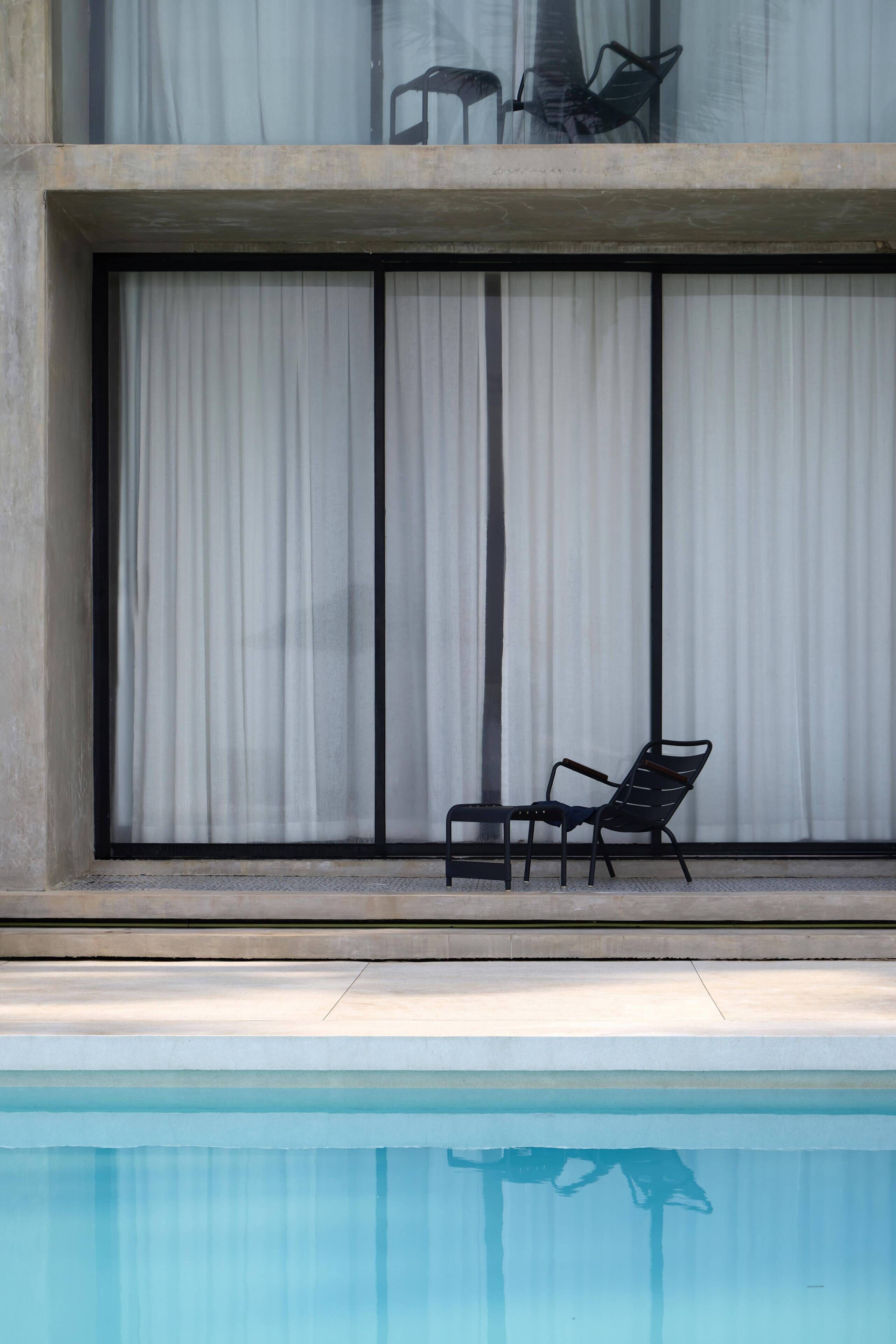 A poolside area with a chair and a large window with curtains.