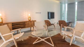 Una sala de estar moderna con una mesa de centro de vidrio, sillas de mimbre, una consola de madera y un televisor de pantalla plana montado en la pared.