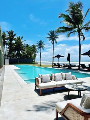 Ein Poolbereich mit einer Sitzecke, Palmen und Blick aufs Meer.