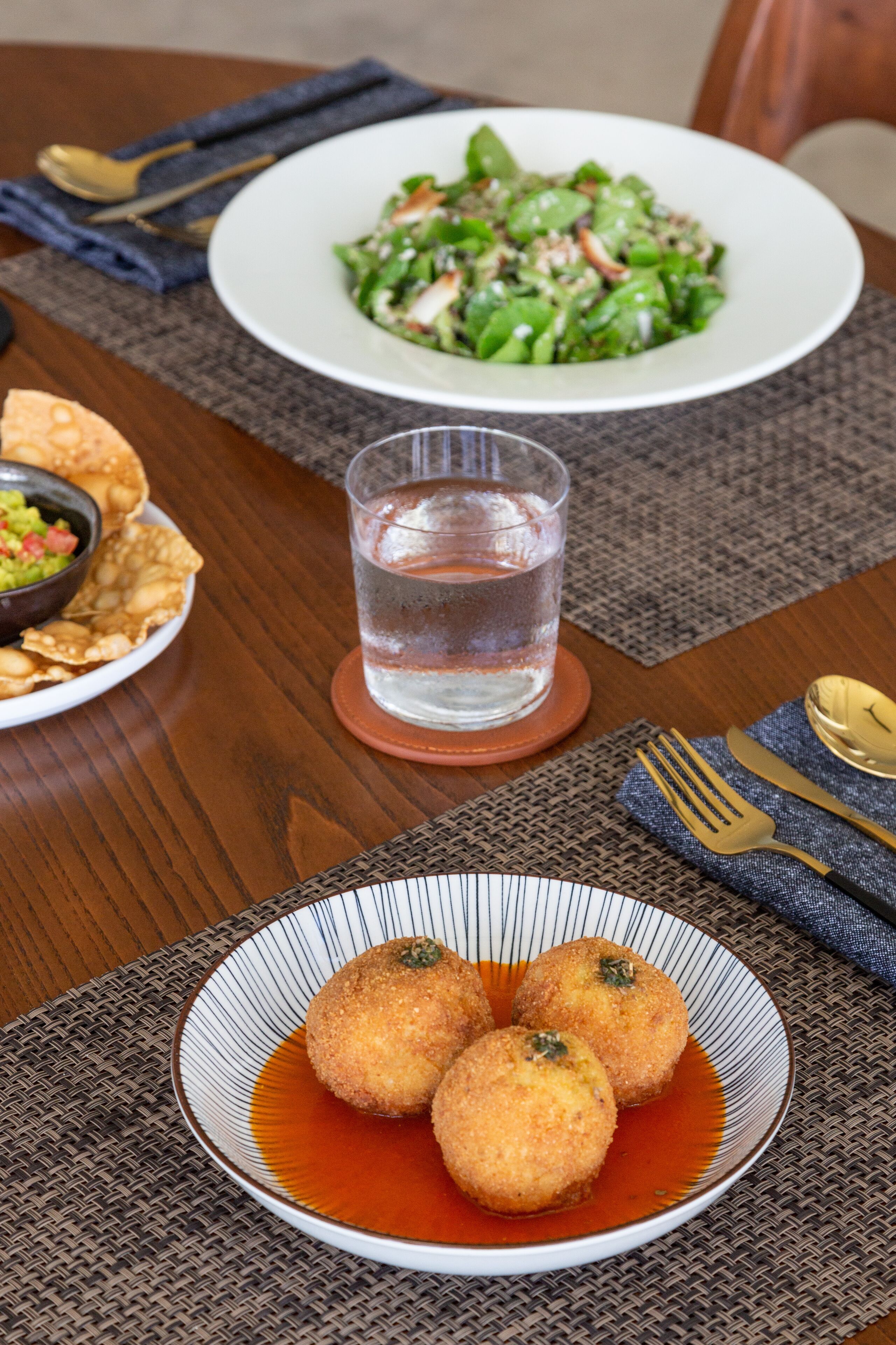 A dining table with a plate of croquettes, a glass of water, and a salad.