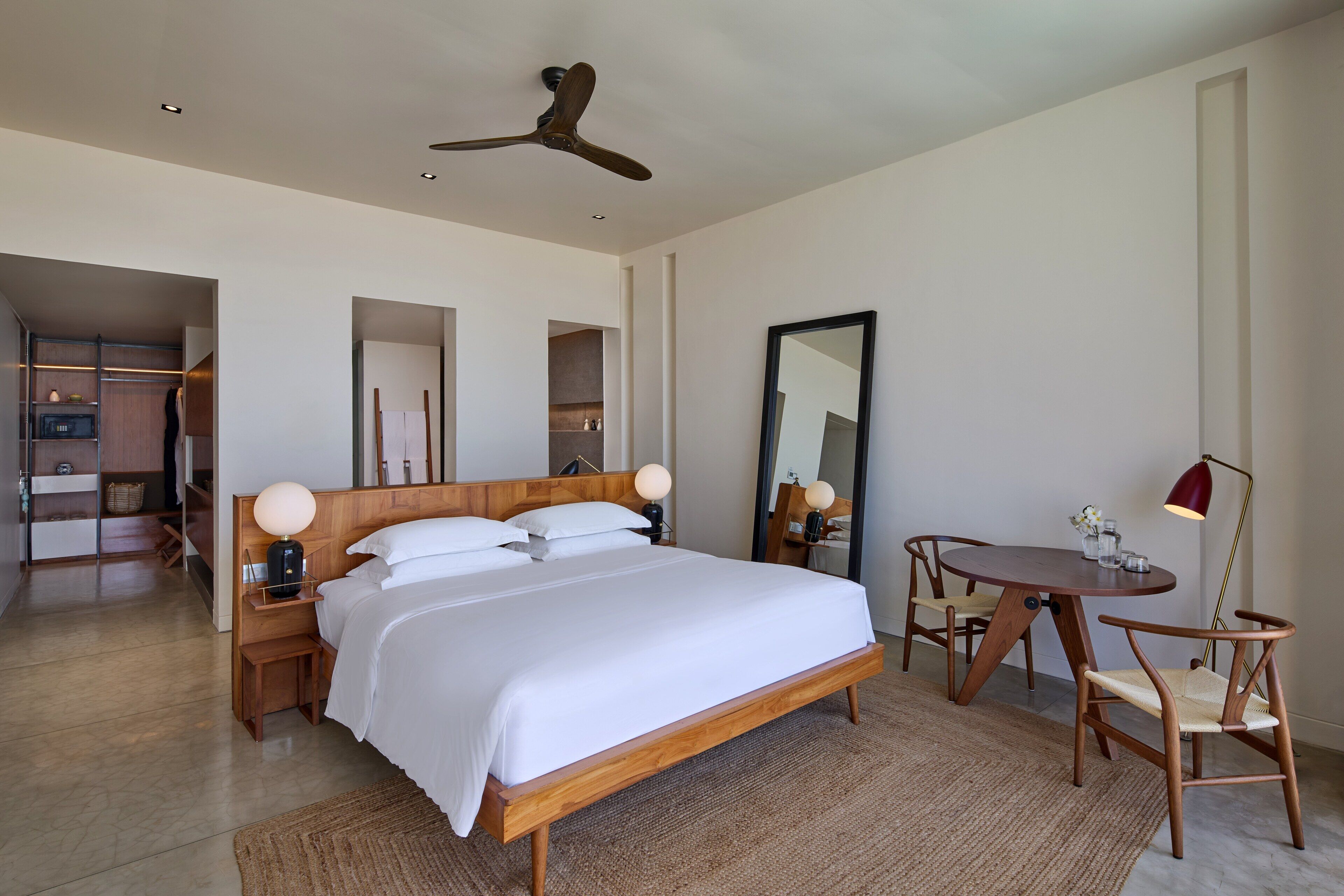A modern hotel room with a wooden bed, a round dining table, and a ceiling fan.