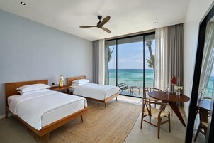 Habitación de hotel con dos camas, un ventilador de techo, una mesa de comedor con sillas y vista al océano.