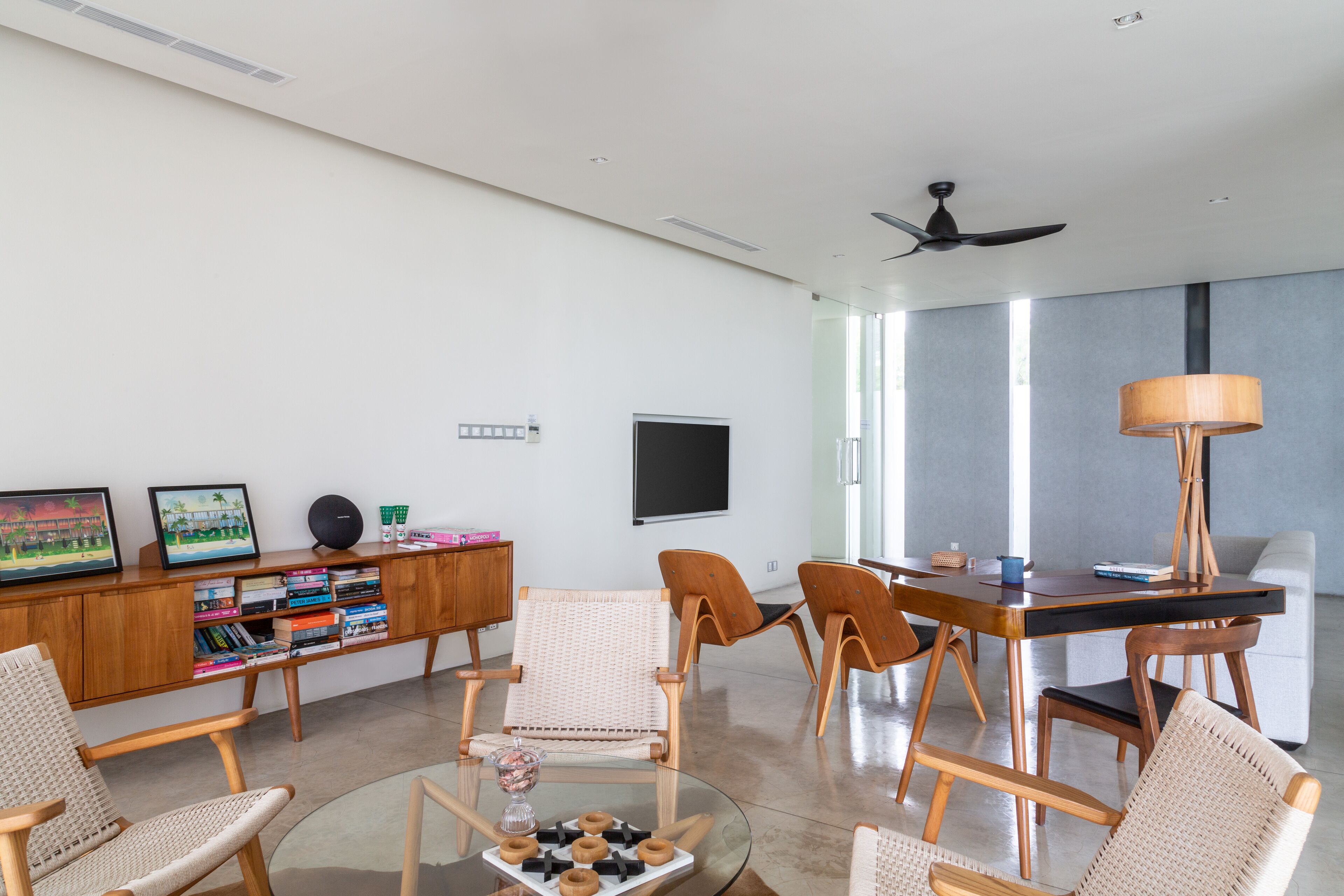 Un salon moderne avec une table basse en verre, des fauteuils en osier, un bureau en bois et une bibliothèque.