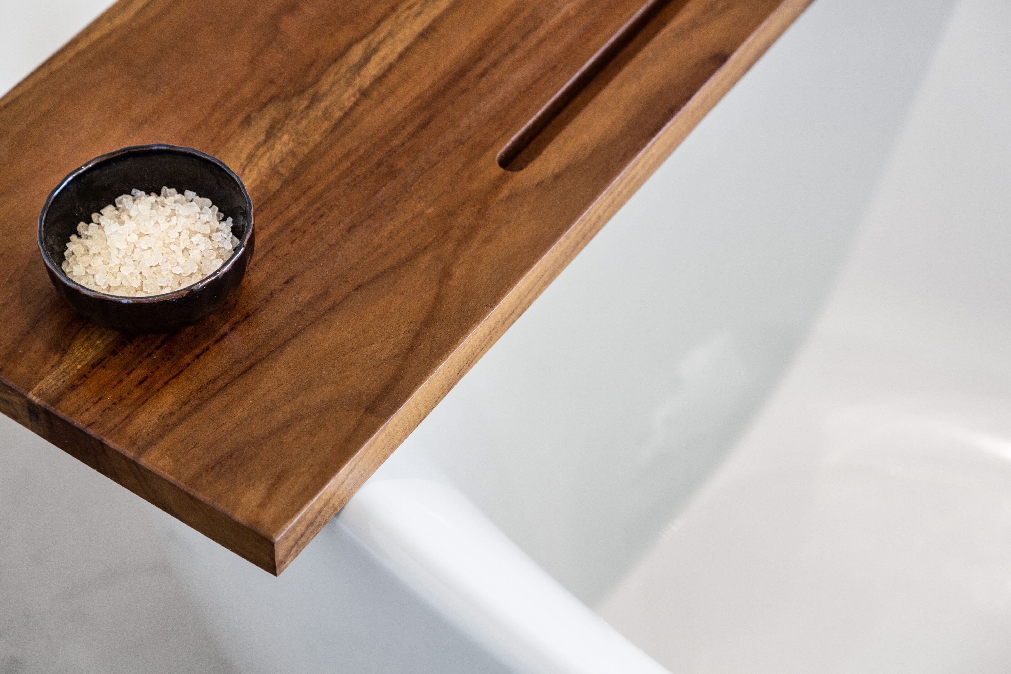 Un plateau en bois sur lequel se trouve un bol de sels de bain blancs, posé sur le comptoir d’une salle de bain.