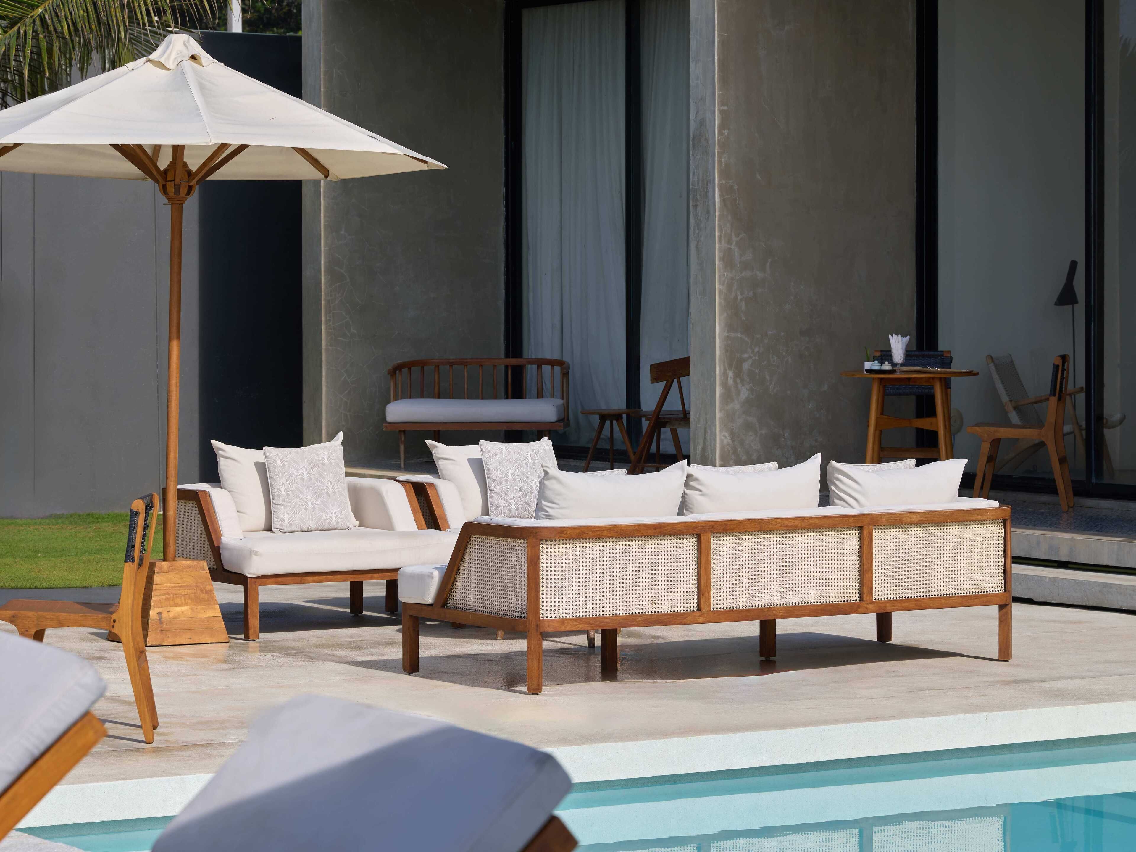Un área junto a la piscina con sillones de descanso, un banco de madera y una sombrilla grande.