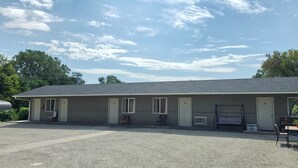 A single-story motel with a gravel driveway and a swing set in the front yard.