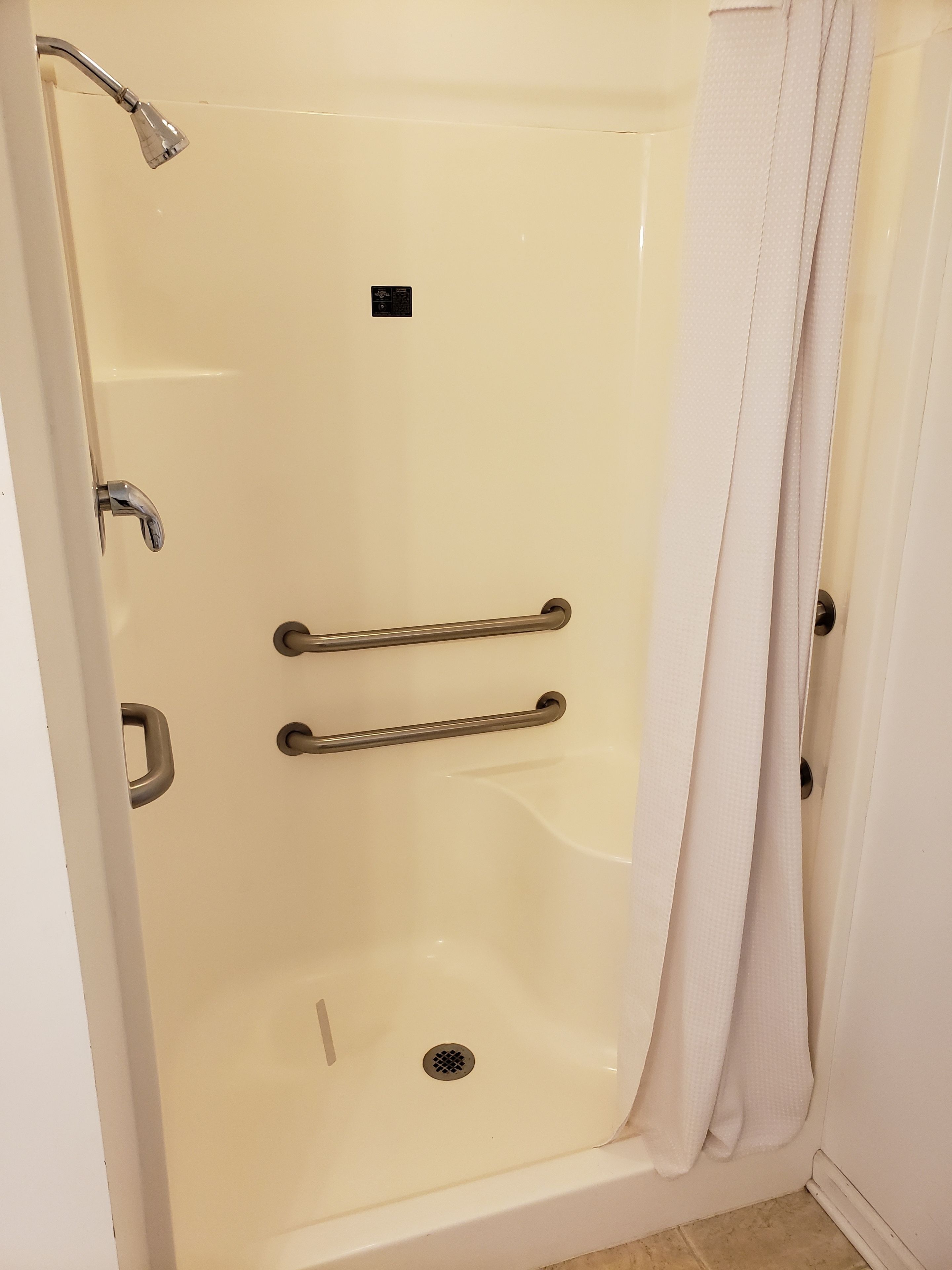 A walk-in shower with a grab bar, a showerhead, and a drain.