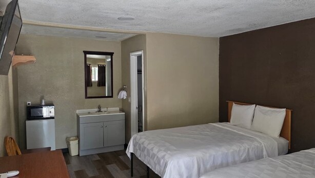 A hotel room with two beds, a small kitchenette, a mirror, and a door leading to another room.