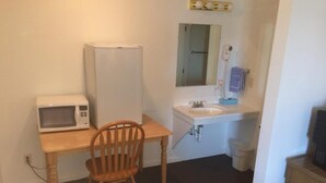 A compact kitchenette with a microwave, sink, and chair.