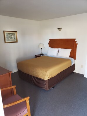 A hotel room with a bed, a nightstand with a lamp, a chair, and a framed picture on the wall.