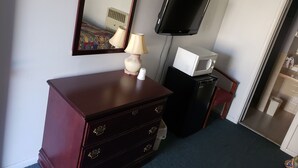 A room with a wooden dresser, a lamp, a microwave, a television, and a mirror.