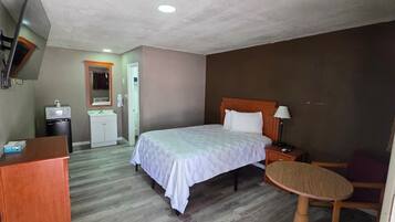 Habitación de hotel con cama, mesita de noche, silla, escritorio y una pequeña zona de kitchenette.