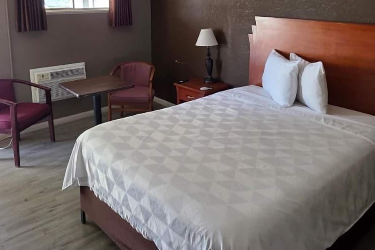 A hotel room with a large bed, a desk, a chair, and a window with curtains.