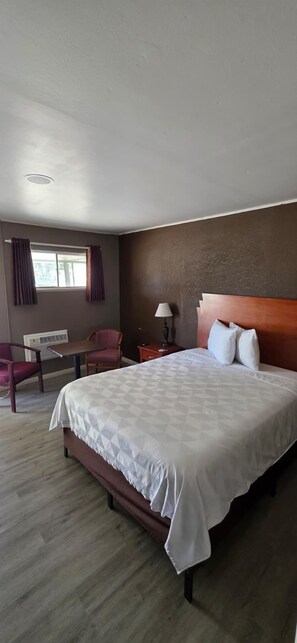 A hotel room with a large bed, a desk, a chair, and a window with curtains.