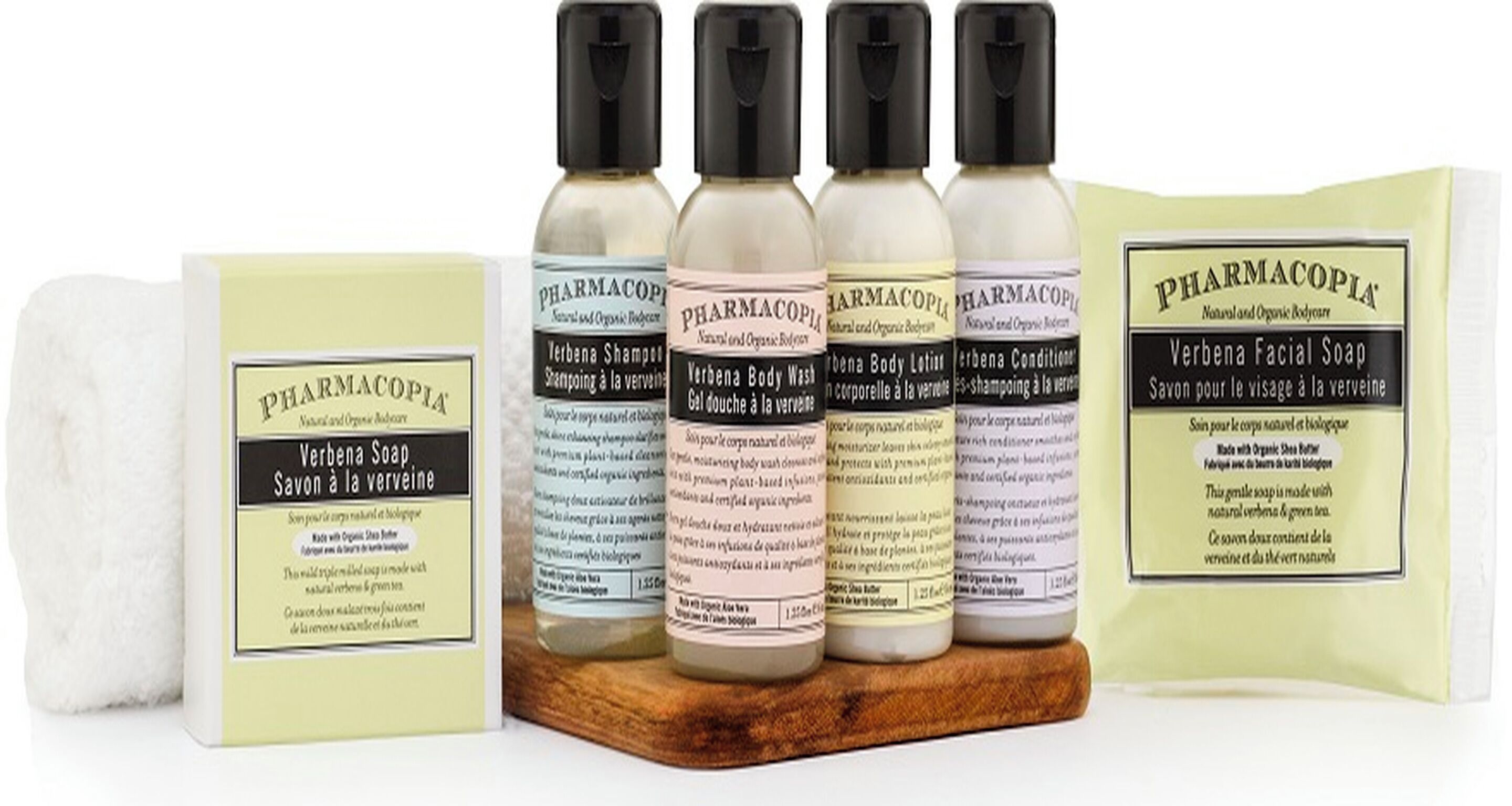 A collection of herbal body care products including soaps, shampoos, and lotions from PHARMACOPIA, displayed on a wooden surface.