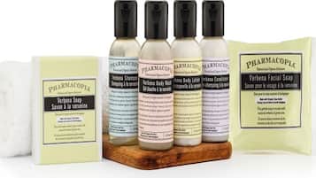 A collection of herbal body care products including soaps, shampoos, and lotions from PHARMACOPIA, displayed on a wooden surface.