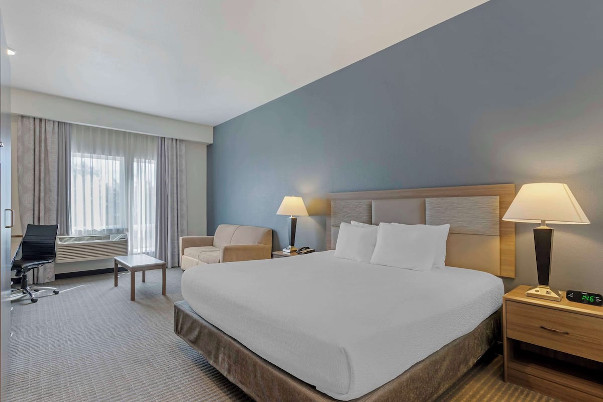 A hotel room with a large bed, two bedside tables with lamps, a desk with a chair, and a window with curtains.