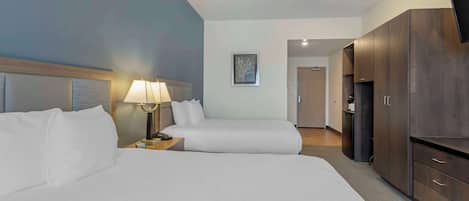 A hotel room with two beds, a nightstand with a lamp, a wardrobe, and a television.