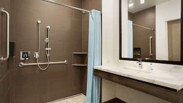 A modern bathroom with a walk-in shower, grab bars, a large mirror, and a white sink.