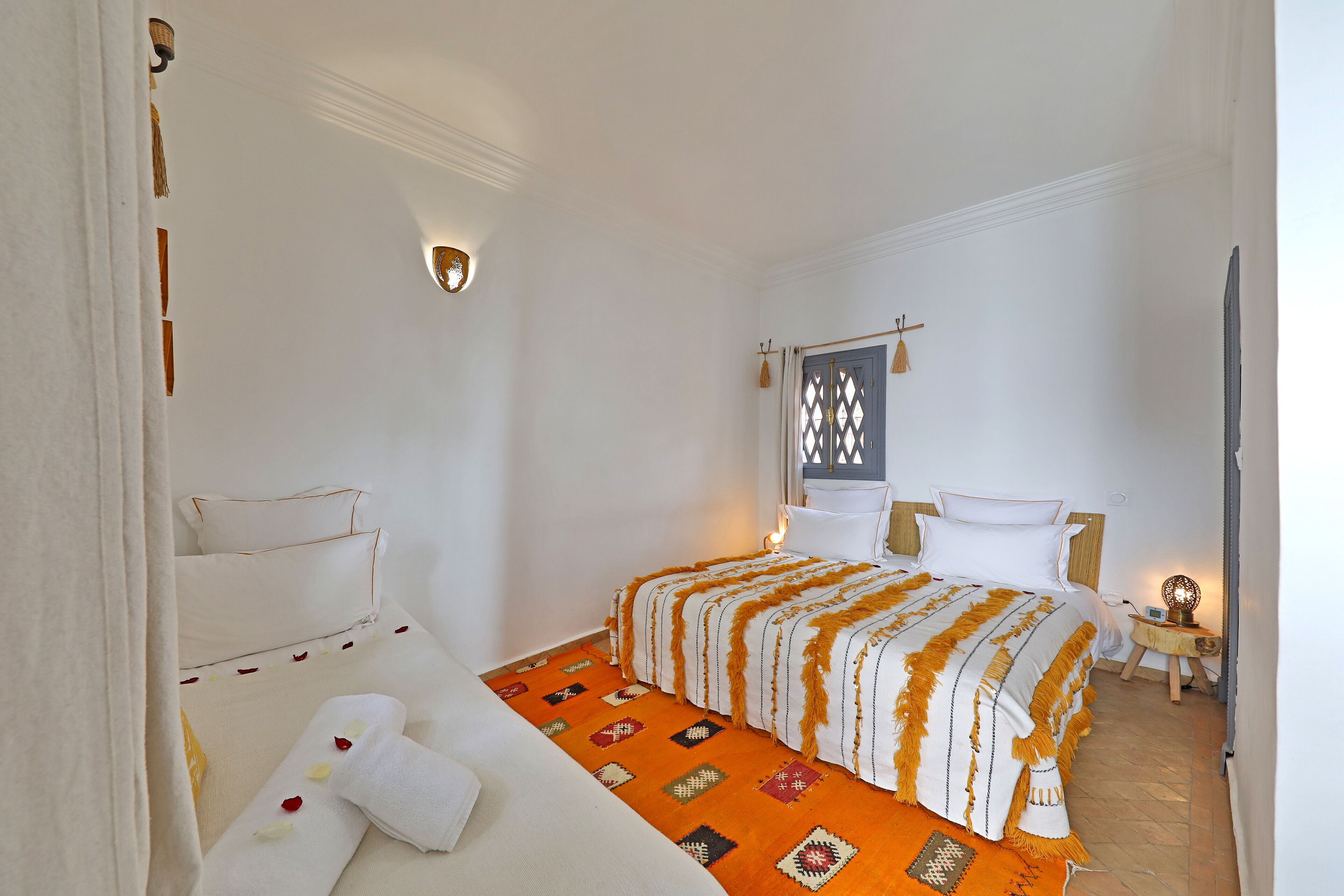 Quarto de hotel com cama, uma pequena mesa com abajur e luminária na parede.