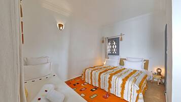 Quarto de hotel com cama, uma pequena mesa com abajur e luminária na parede.