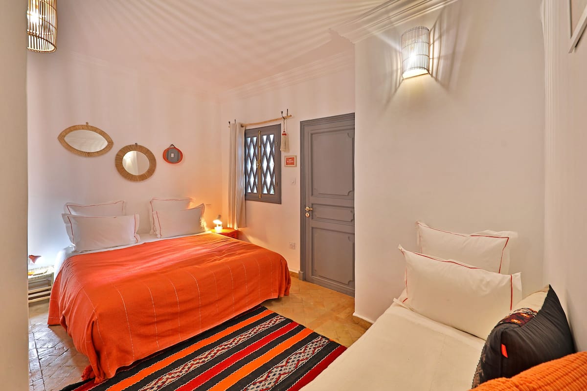 Quarto com uma cama grande, duas mesas de cabeceira, uma janela com um painel decorativo e uma porta com puxador.