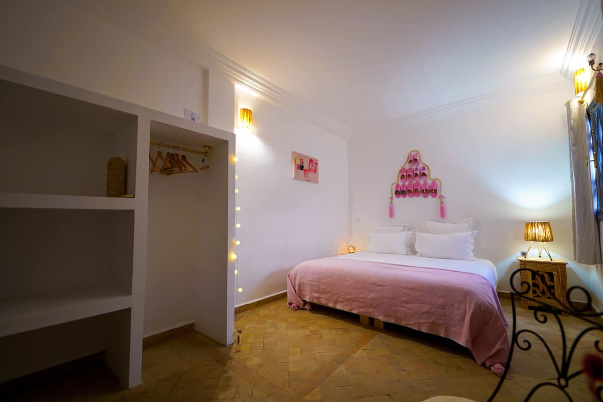 Quarto com cama, guarda-roupa, penteadeira com iluminação e um objeto decorativo na parede.