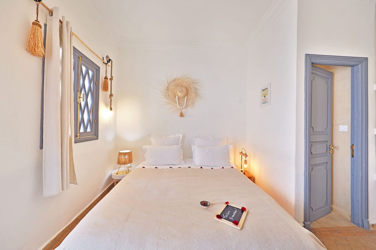 Quarto bem arrumado com uma cama, abajures, um enfeite na parede e uma porta.
