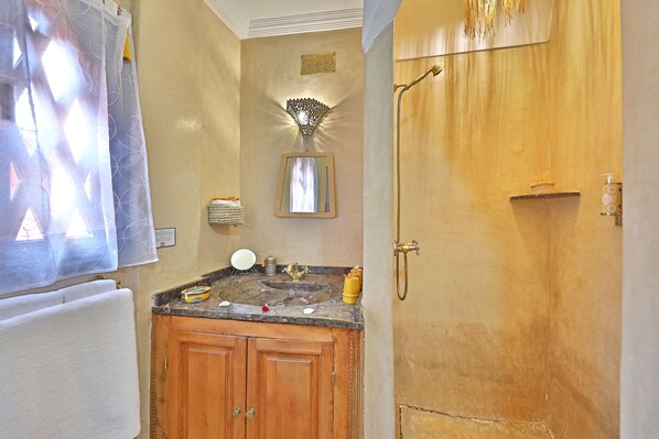 A bathroom with a wooden vanity, a sink, a mirror, and a shower area.