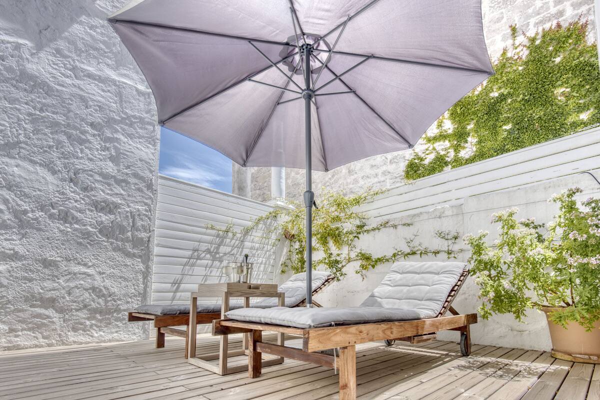 A wooden deck with two lounge chairs and a large umbrella.