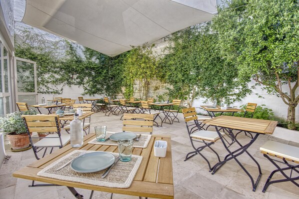 An outdoor patio area with multiple wooden tables and chairs, some with table settings. - Can Albertí 1740 Hotel Boutique (Mahón)