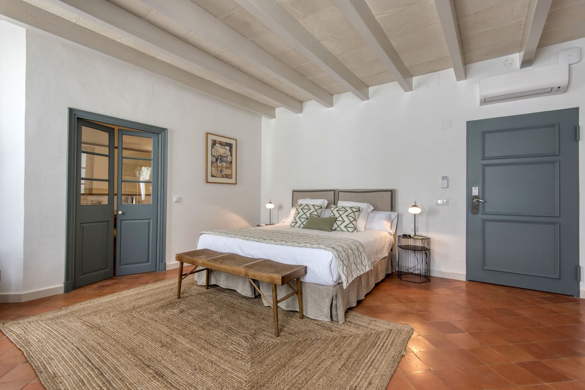 A bedroom with a bed, bedside tables, a bench, and a door.