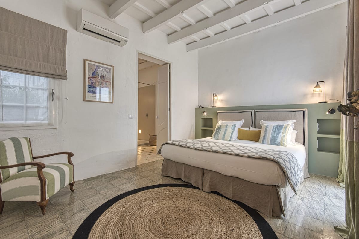 A bedroom with a bed, a chair, a rug, a wall-mounted shelf, and a poster.