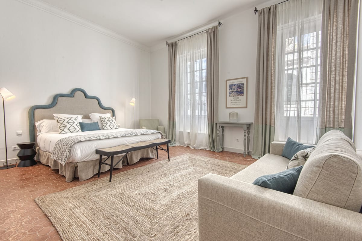 A bedroom with a bed, bedside tables, a bench, a sofa, and a fireplace.