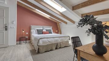 Un dormitorio con cama, una mesa de madera, una silla, una planta en maceta y un tragaluz.