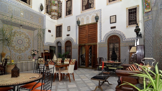 Um interior tradicional marroquino com um pátio ladrilhado, móveis de madeira e detalhes ornamentais em azulejos.