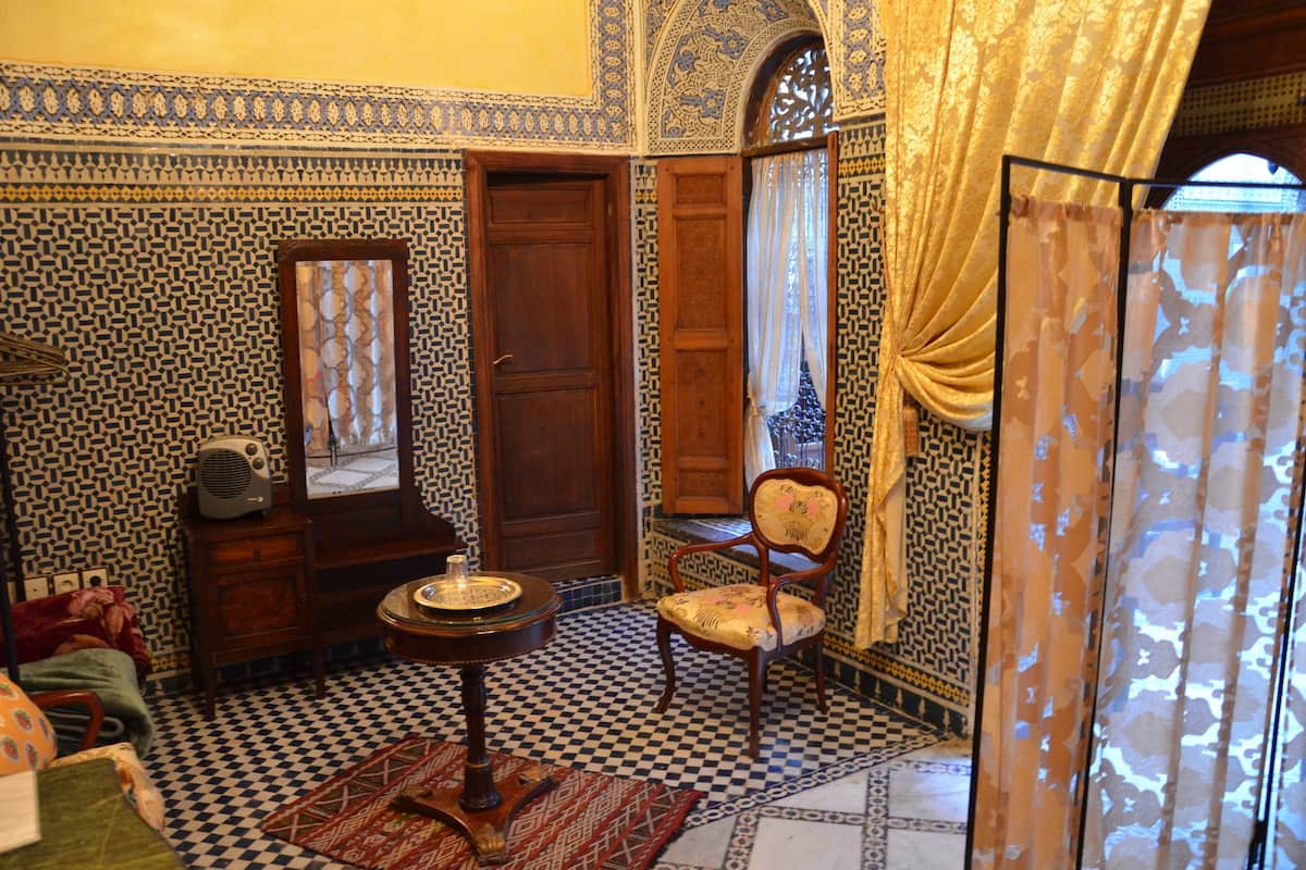 Une pièce avec un sol à carreaux, une porte en bois, une chaise, une petite table et un miroir.