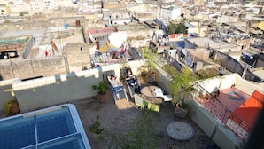 Terraço no telhado com área de estar ao ar livre, plantas em vasos e vista da área urbana circundante.