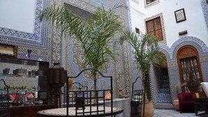 Um interior marroquino tradicional com trabalhos em azulejos detalhados, uma área de estar e uma exposição de artefatos locais.