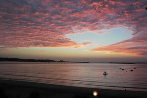 Un coucher de soleil sur une vaste étendue d’eau, avec des bateaux et une côte lointaine.