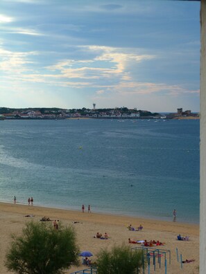 Une plage où des gens se prélassent au soleil et se baignent, un ciel dégagé et des bâtiments en arrière-plan.
