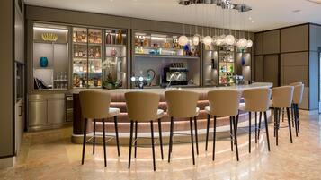 Un bar moderno con barra curva, diversas opciones de asientos y una amplia variedad de botellas y cristalería a la vista.