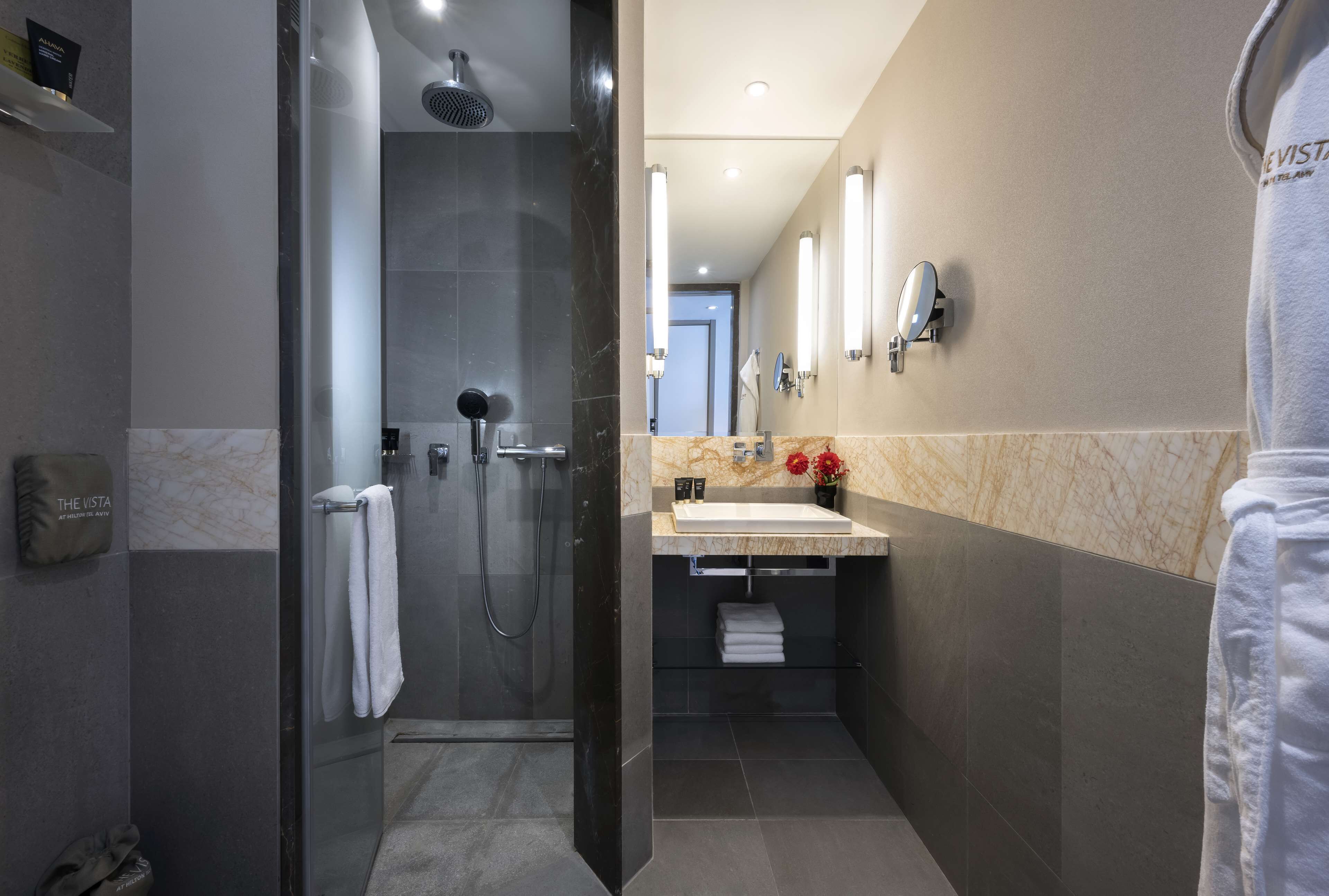 Un baño moderno con cabina de ducha de vidrio, lavamanos con encimera de mármol y un perchero para toallas.