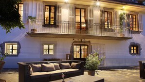 Een gebouw met twee verdiepingen, een balkon en een stenen terras, met een grote bank.