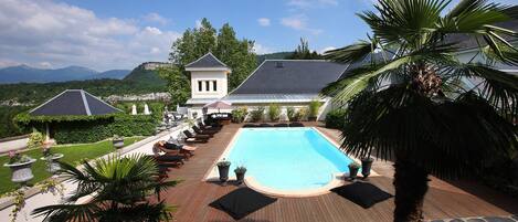 A pool area with lounge chairs, a stone deck, and a view of a mountain and town in the background.
