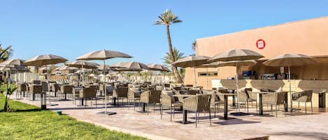 An outdoor seating area with numerous tables and chairs, umbrellas, and a bar sign.