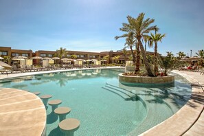 A pool area with lounge chairs and umbrellas, surrounded by palm trees and a building with multiple windows. - Be Live Collection Marrakech Adults Only - All Inclusive (Marrakech)