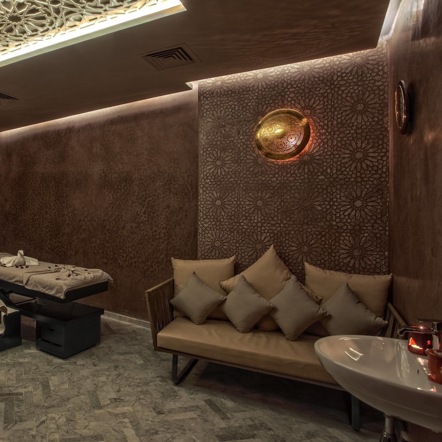 A spa room with two massage tables, a sofa with cushions, a sink, and a decorative ceiling light.