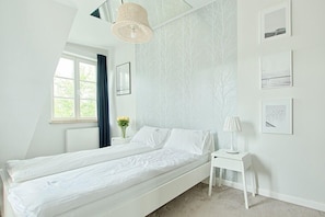 A bedroom with a bed, a bedside table with a lamp, a window with curtains, and wall-mounted pictures. - Imperial Apartments - Valor (Sopot)