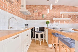 A modern kitchen with white cabinets, a wooden countertop, and a brick wall. There is a sink, a stove, and a chair with a cushion. - Imperial Apartments - Valor (Sopot)